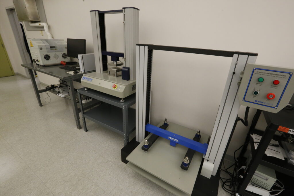 An industrial laboratory setup featuring two Haida International material testing machines for compression and tensile strength, alongside a computer workstation, suggesting a quality control or research environment.