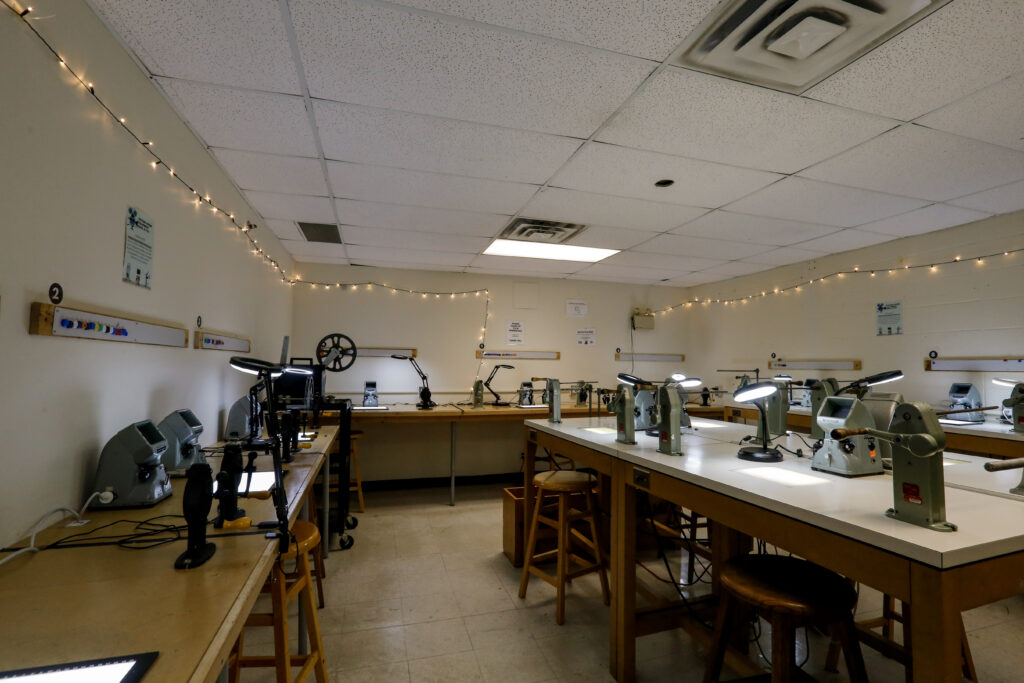 An empty film editing classroom featuring long tables equipped with film viewers, desk lamps, and various tools, decorated with string lights along the walls.