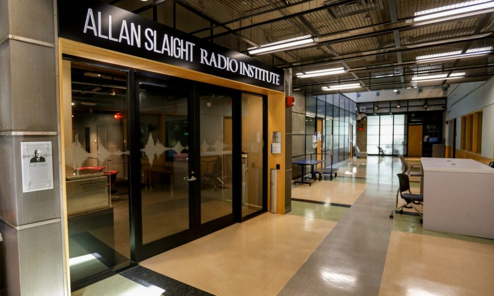 Entrance to the Allan Slaight Radio Institute, featuring glass doors, a reception desk on the right, and a modern interior with bright overhead lighting.